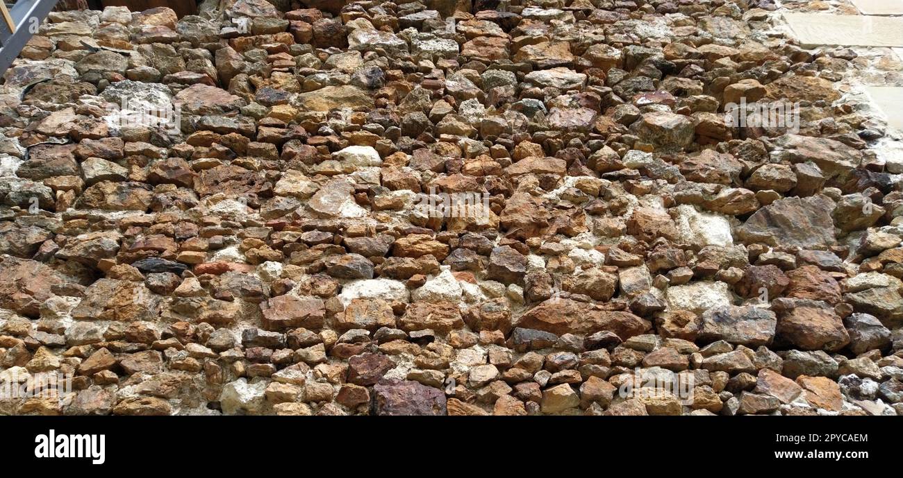 Stone wall. Stacked large bricks and cobblestones in warm colors. Loose white stones protruding from the surface of the wall. Stock Photo