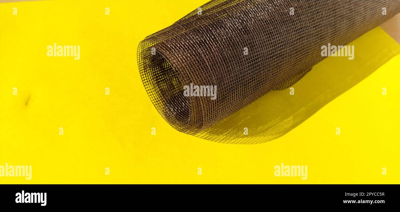 Roll of window screen, closeup. Roll of brown mosquito nets. Barrage mesh. Grid on yellow background Stock Photo