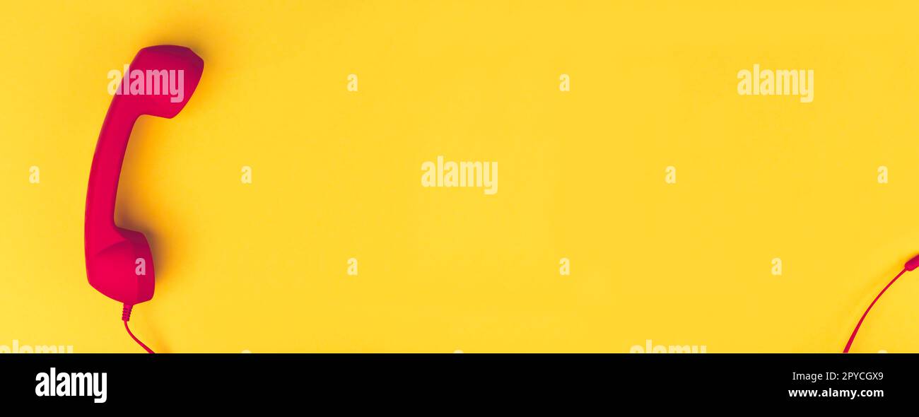 Red landline telephone receiver in front of yellow background