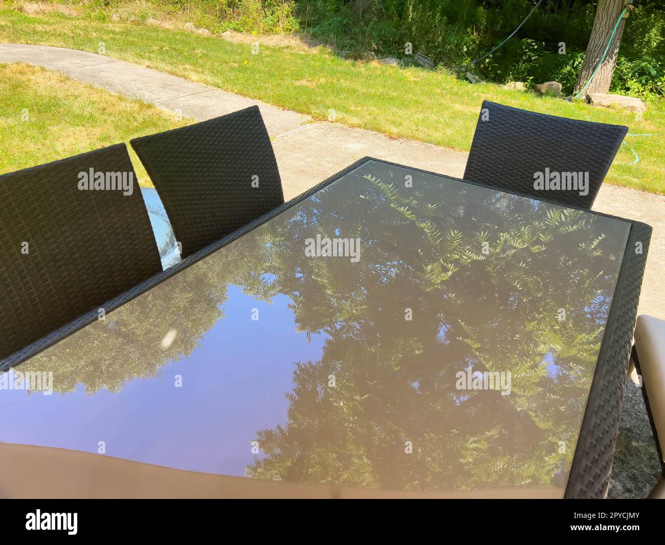 Outdoor glass table reflects overhead trees on sunny day Stock Photo