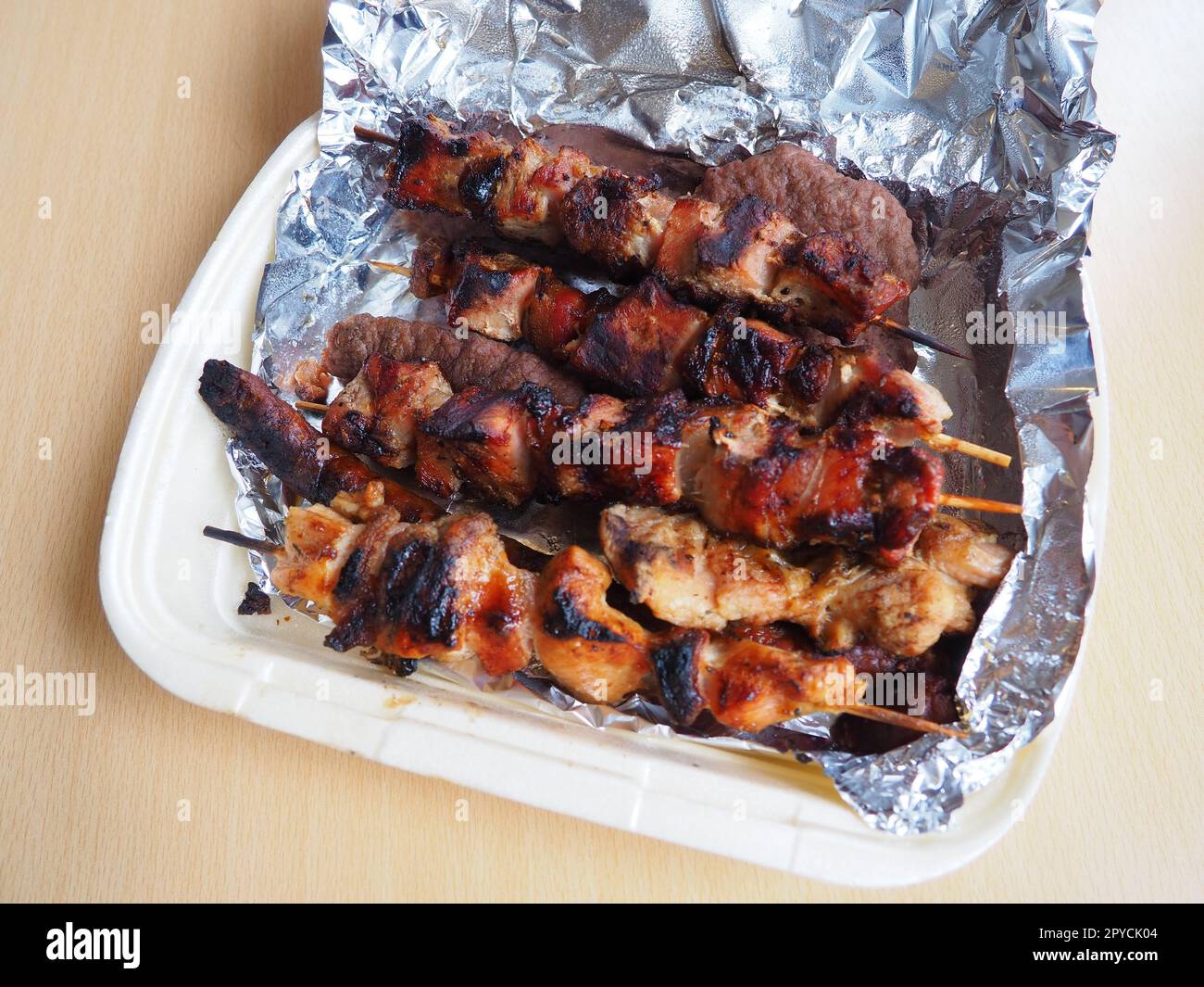 Grilled meat in disposable packaging and aluminum foil, delivered from a restaurant. Food delivery home from restaurants and cafes. Shish kebab and lumpy meat of chicken, pork and lamb Stock Photo