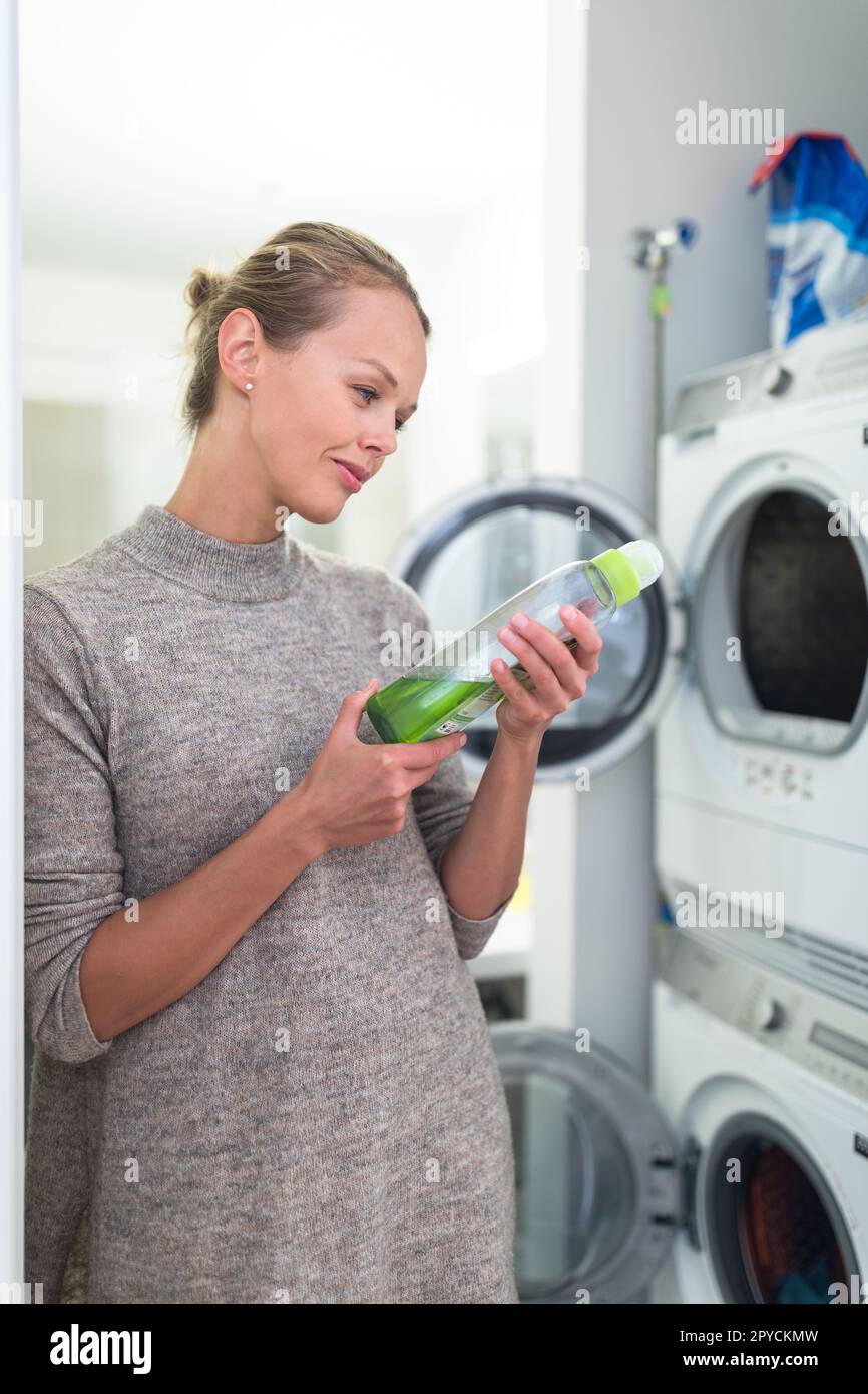 Pretty, young woman doing laundry at home. Choosing carefully the washing product to wash her clothes well and responsibly towards the environment Stock Photo