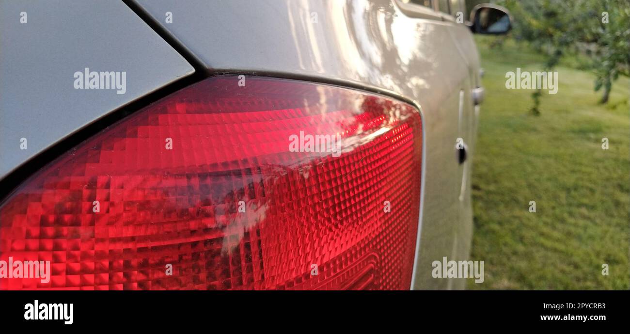 Detail of the rear end of a silver car with focus on the brake lights. Red rear light of the car. Brake signal for the driver driving behind Stock Photo