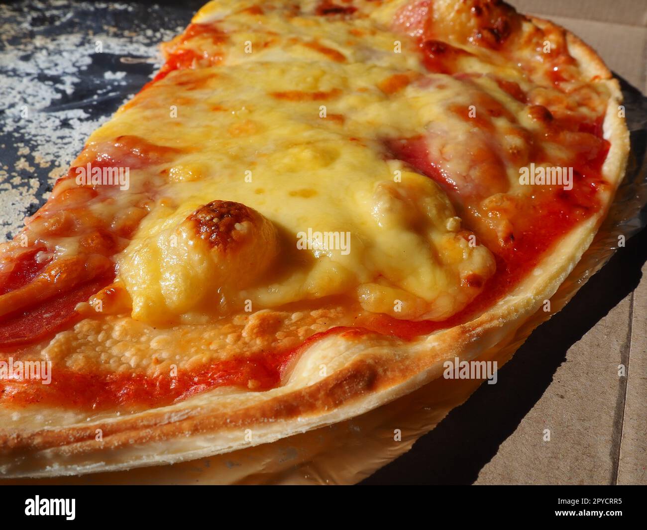 Pizza with tomatoes and cheese in a cardboard box and aluminum foil. Delicious pizza close up. Courier delivery of food to your home. Ordering pizza. Traditional Italian round yeast cake with filling Stock Photo