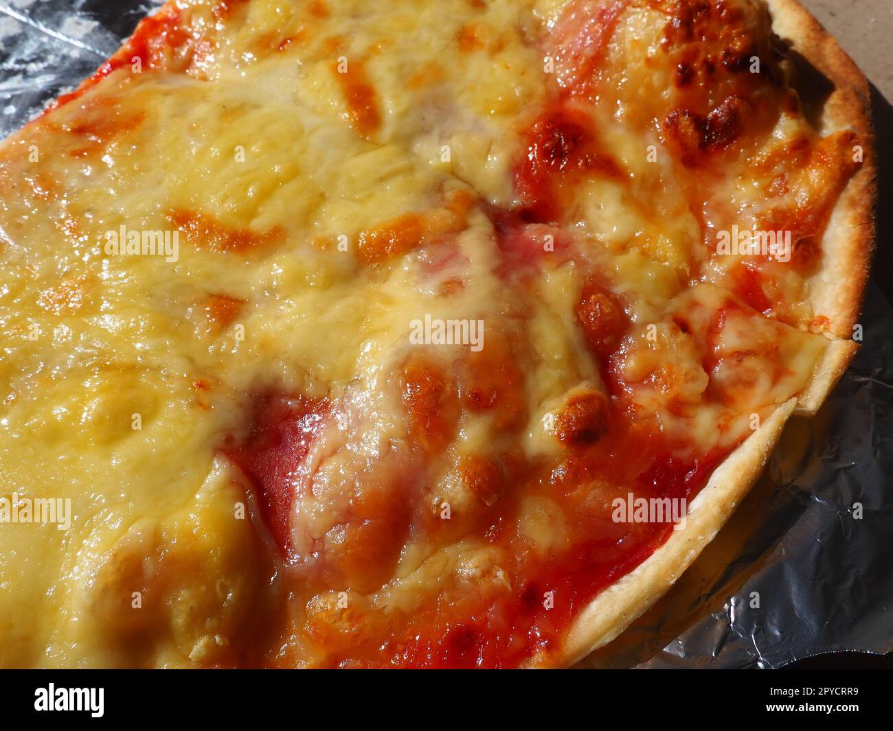 Pizza with tomatoes and cheese in a cardboard box and aluminum foil. Delicious pizza close up. Courier delivery of food to your home. Ordering pizza. Traditional Italian round yeast cake with filling Stock Photo