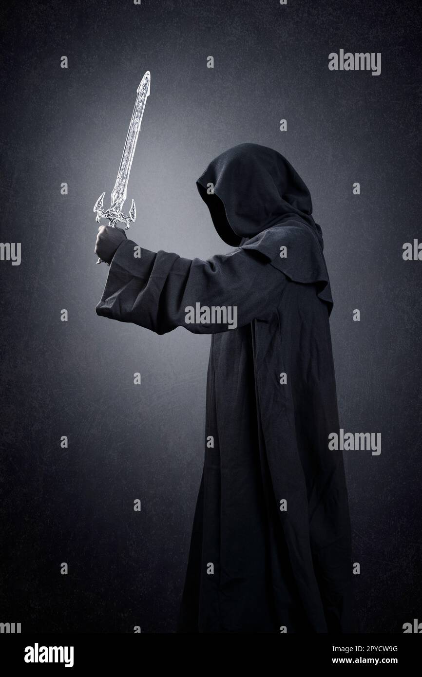 Dark knight with hooded cape and medieval sword over dark misty background Stock Photo