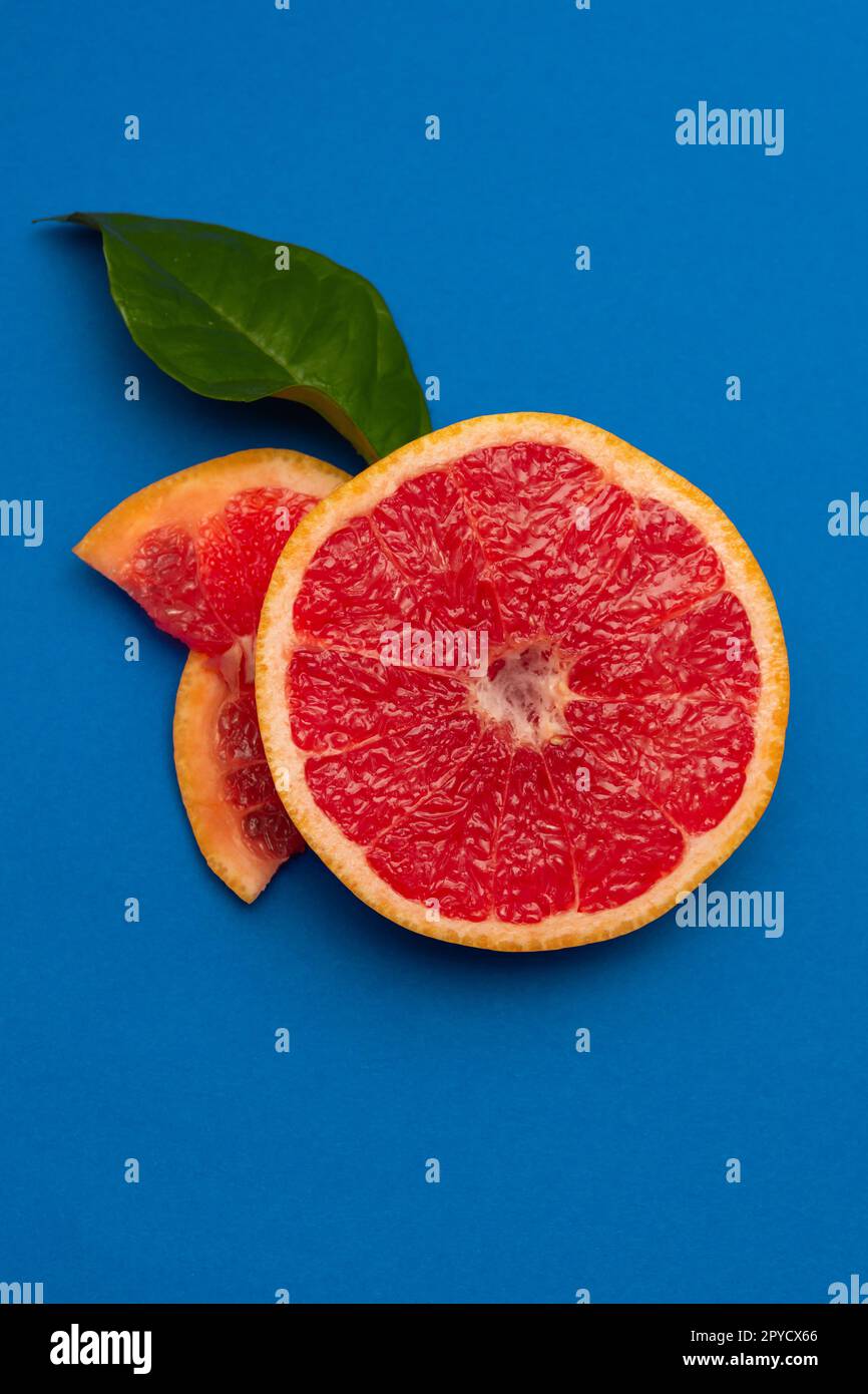 Sliced sides of a grapefruit, three pieces with a green leaf, red pulp isolated on a blue background, vertical shot Stock Photo