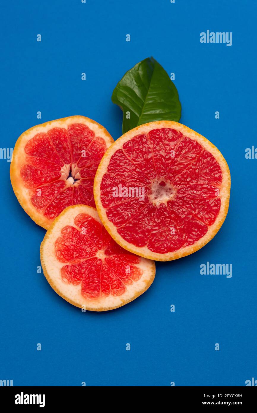 Sliced sides of a grapefruit, three pieces with a green leaf, red pulp isolated on a blue background, vertical shot Stock Photo