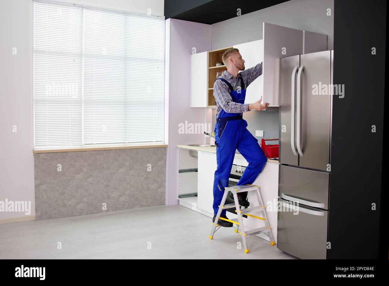 Male Carpenter Assembling White Cabinet On Wall Stock Photo