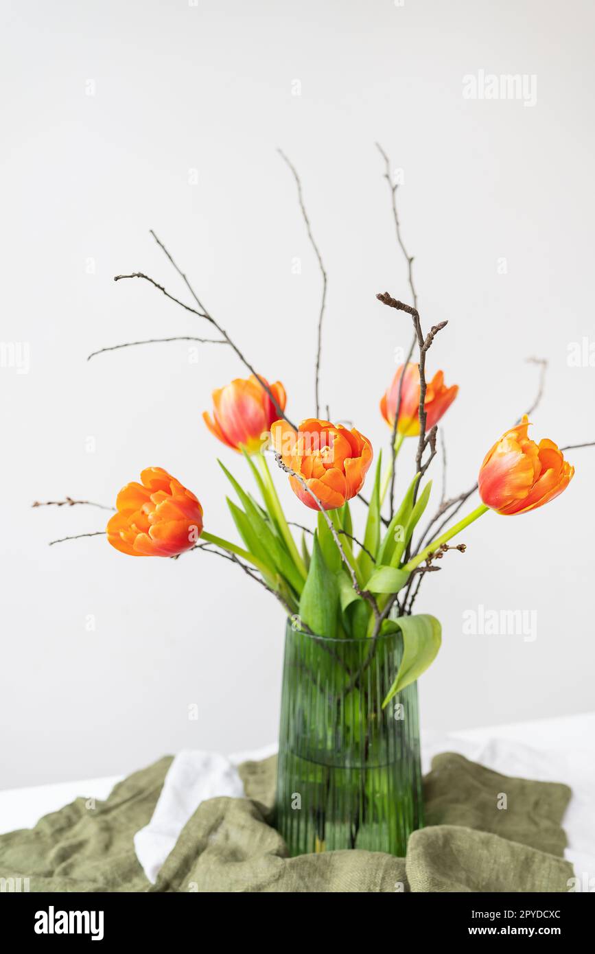 A very beautiful spring bouquet in a green vase stands on a table on a linen tablecloth, orange peony tulips. Mother's Day, March 8, Valentine's Day. Stock Photo