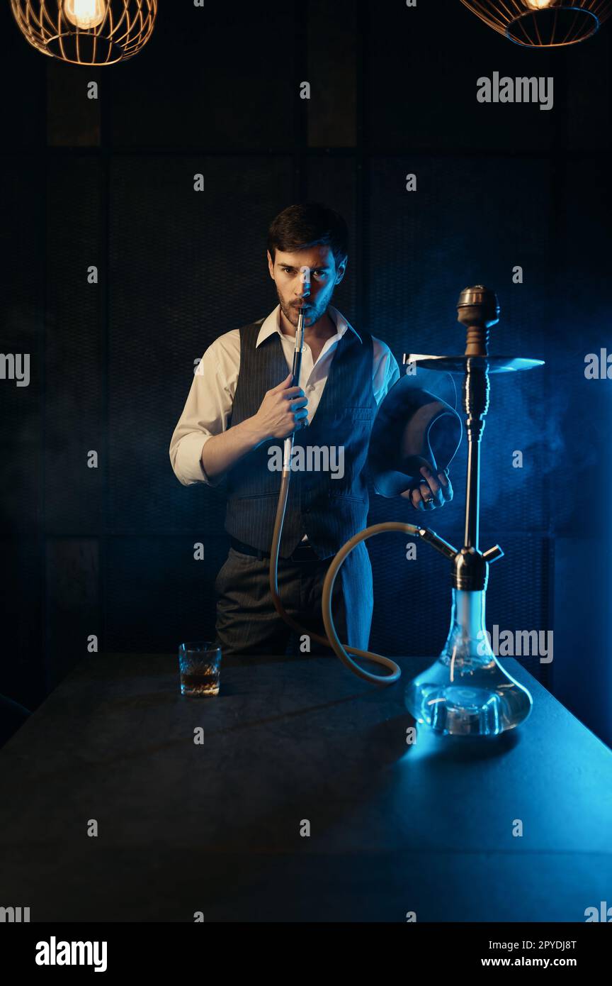 Retro dressed guy smoking hookah while standing in clouds of smoke