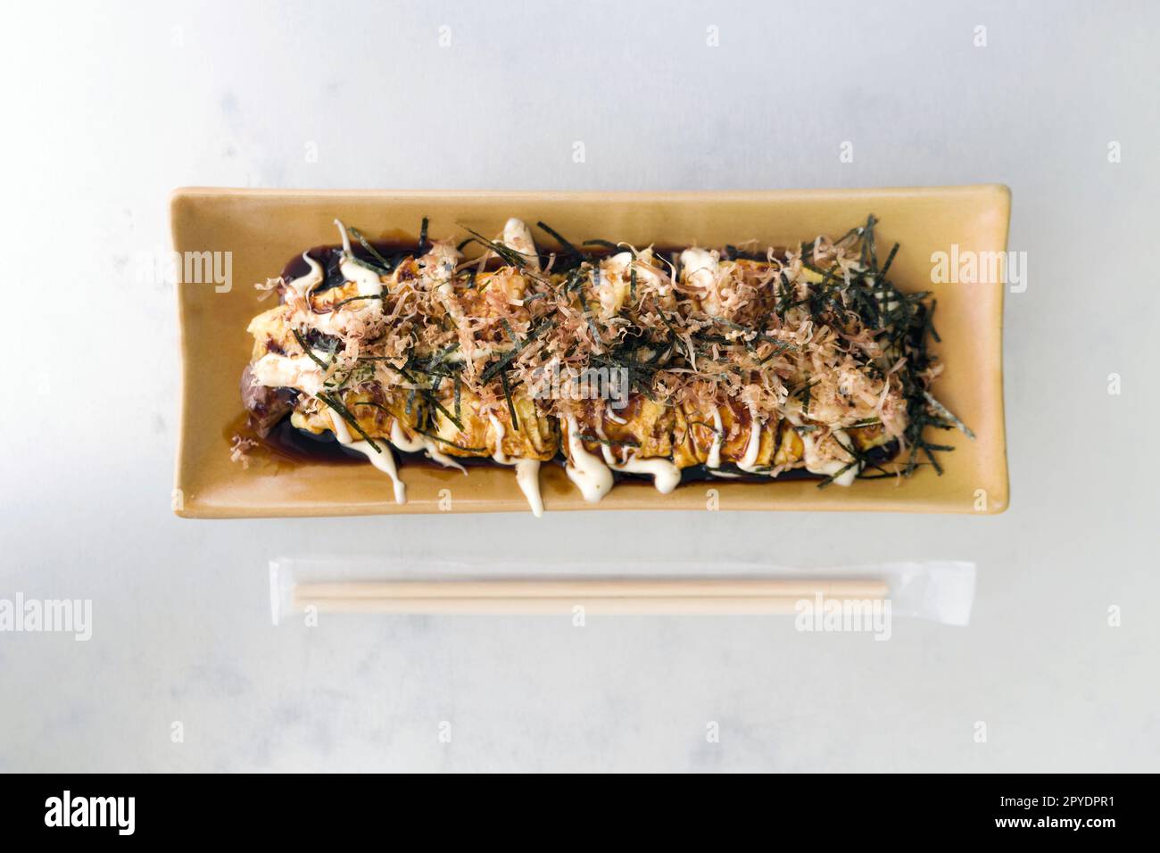 Gyuhei Yaki, stir fried vegetable wrapped with egg and meat on ceramic plate place next to bamboo chopstick on white table. Top View Stock Photo