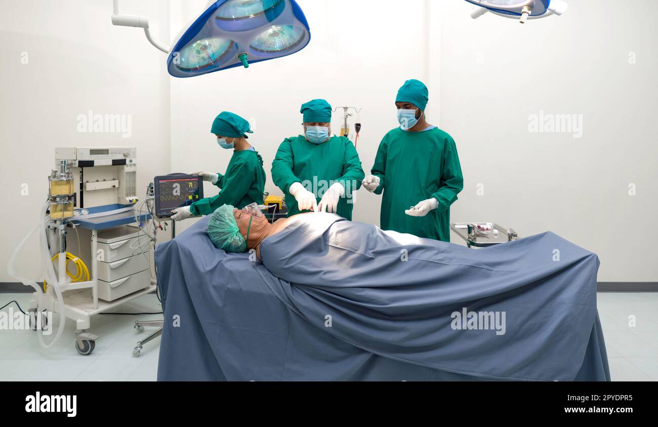 Group of surgeons and nurse in surgical green gown uniform performing surgical operation in operating room. Stock Photo