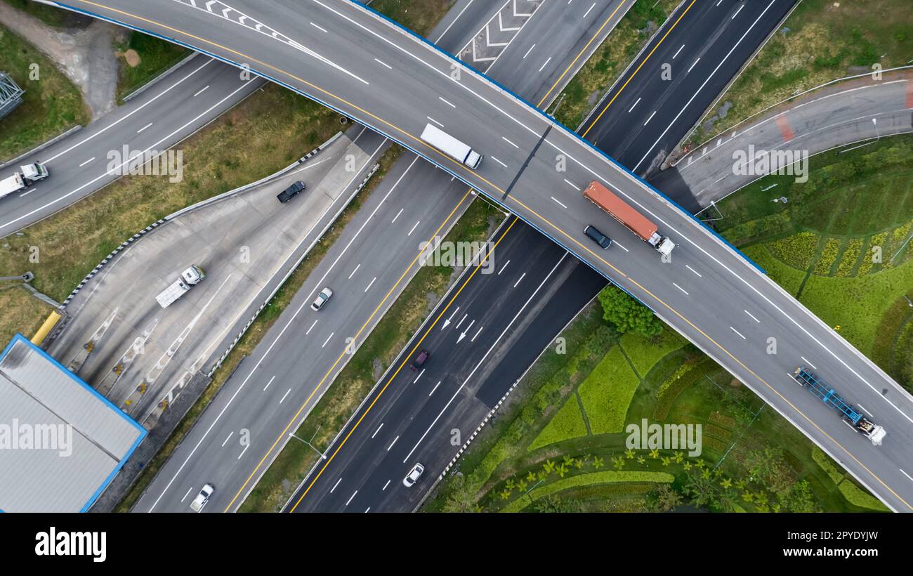 Aerial top view of highway junction interchange road. Drone view of the elevated road, traffic junctions, and green garden. Transport trucks and cars driving on highway. Infrastructure in modern city. Stock Photo