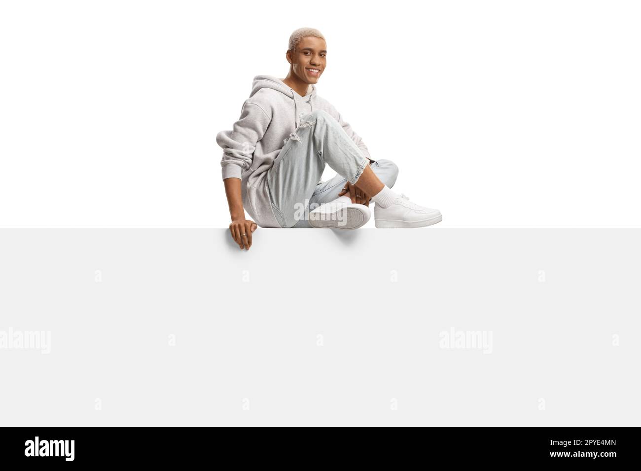 African american gen z guy with bleached hair sitting on a blank panel isolated on white background Stock Photo