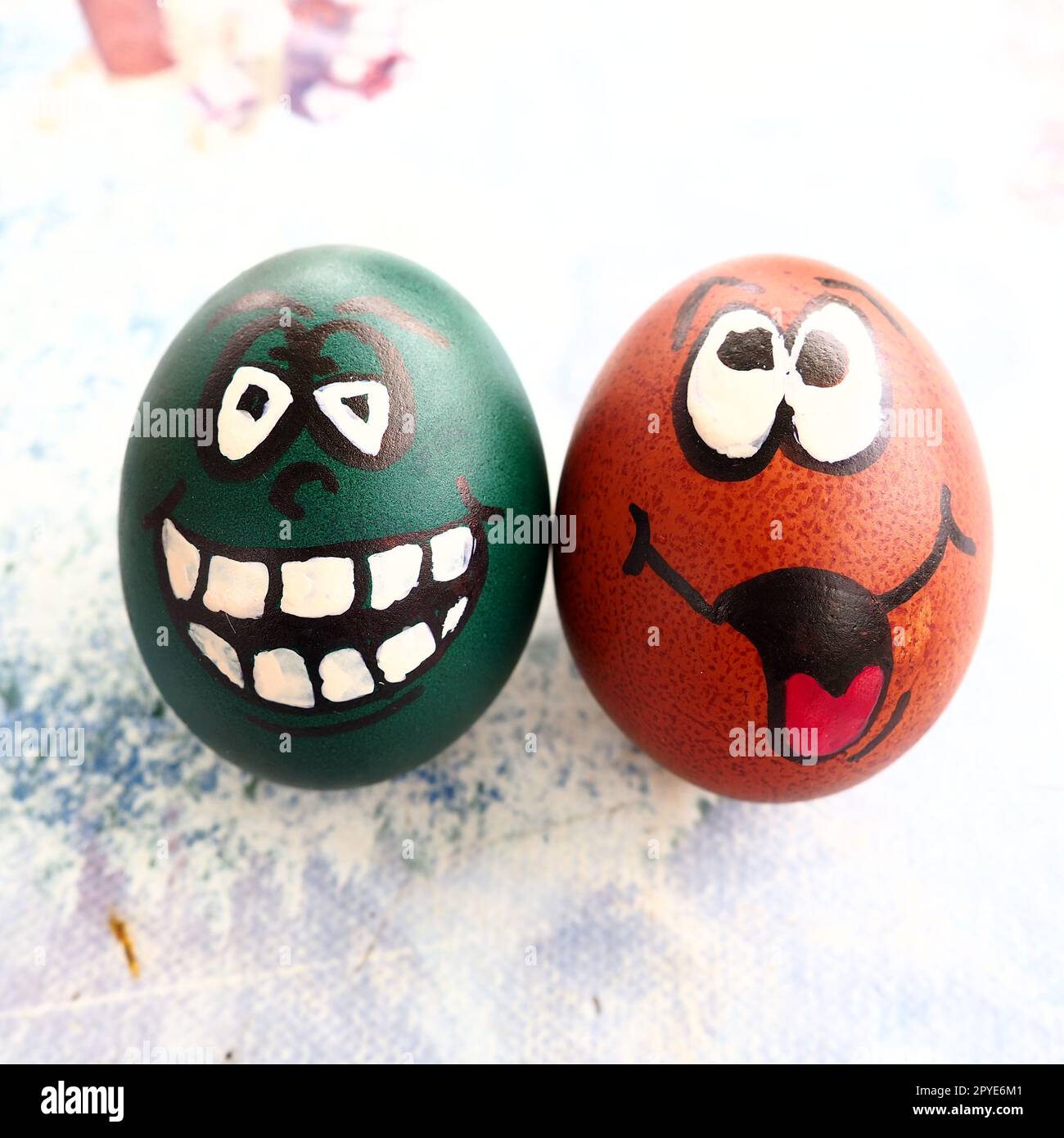 Easter eggs dyed green and brown with painted laughing faces. Funny grimaces with eyes, tongue and big white teeth. Scary face for Halloween. Emoticon for Easter. Light abstract background. Stock Photo