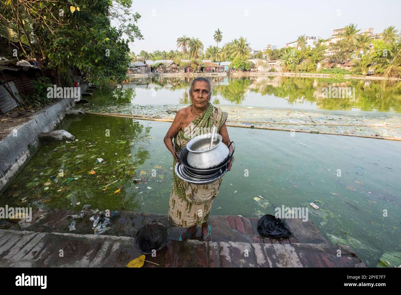 Bangladesh, Khulna, Sonadanga.A woman cleans her pots in the polluted pond water near her home. March 19, 2017. Editorial use only. Stock Photo