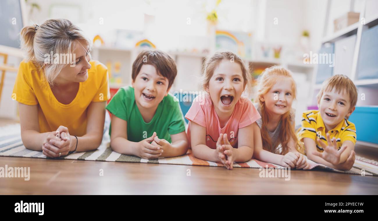 Group of children and teacher lying on the floor and looking in the camera. Stock Photo