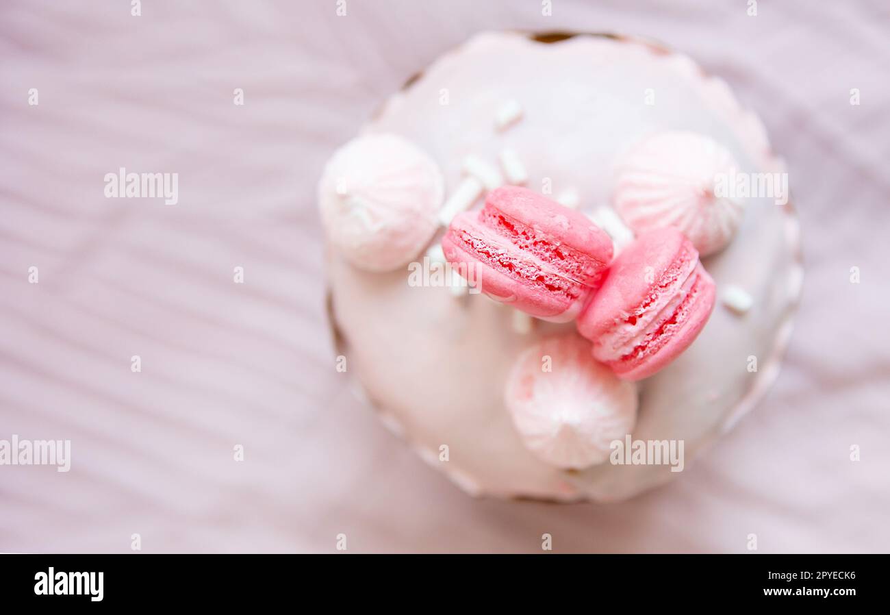 A traditional paska decorated with pink swiss chocolate and meringue stands on a pink tablecloth. Easter holiday, top view. Place for writing. Stock Photo