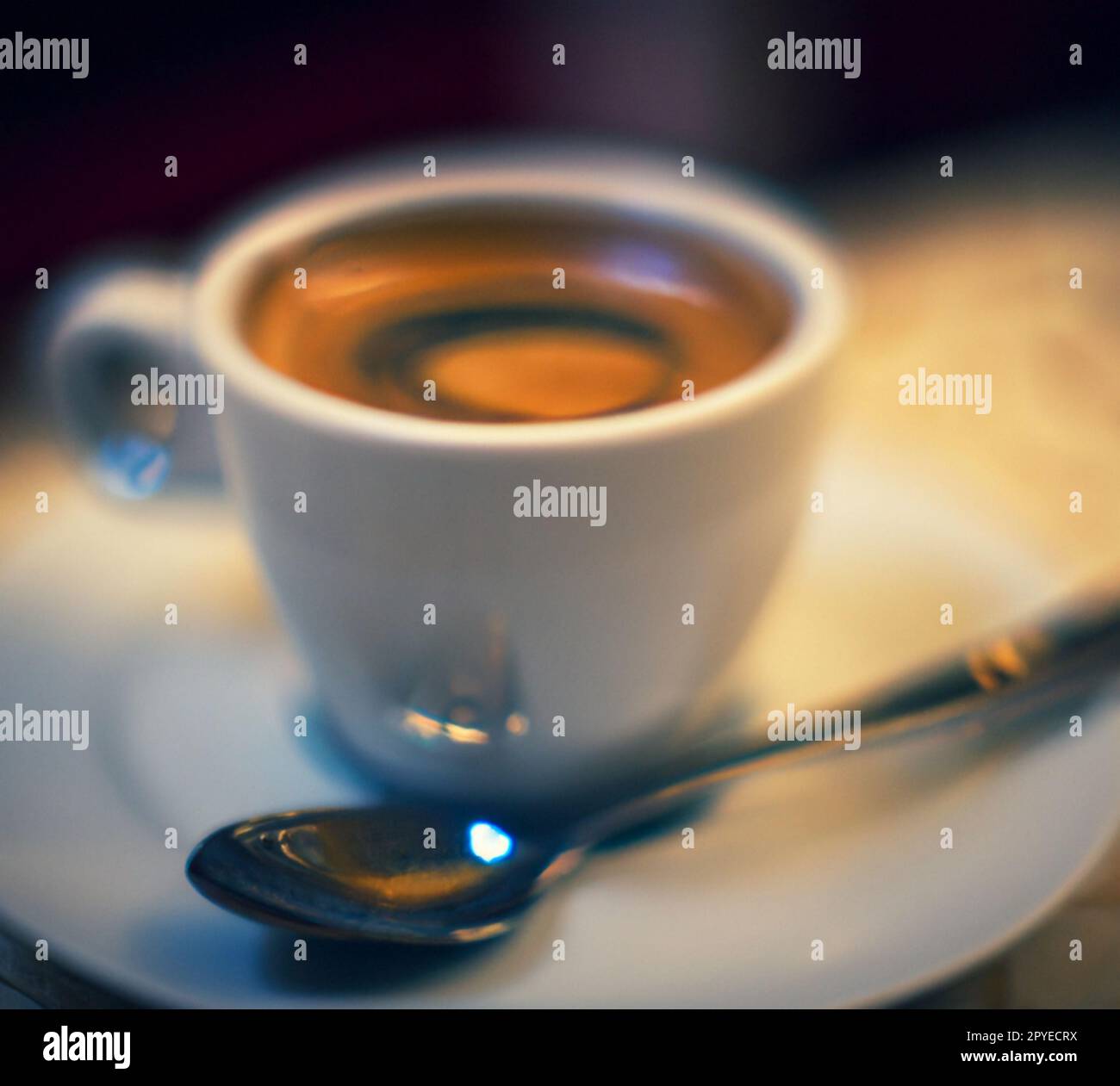 Cup of coffee in cafe. Anamorphic bokeh effect. Tilt-shift photo. Hot coffee  in a white cup with a saucer and a spoon. The coffee is getting cold. Aroma  of coffee beans. Label