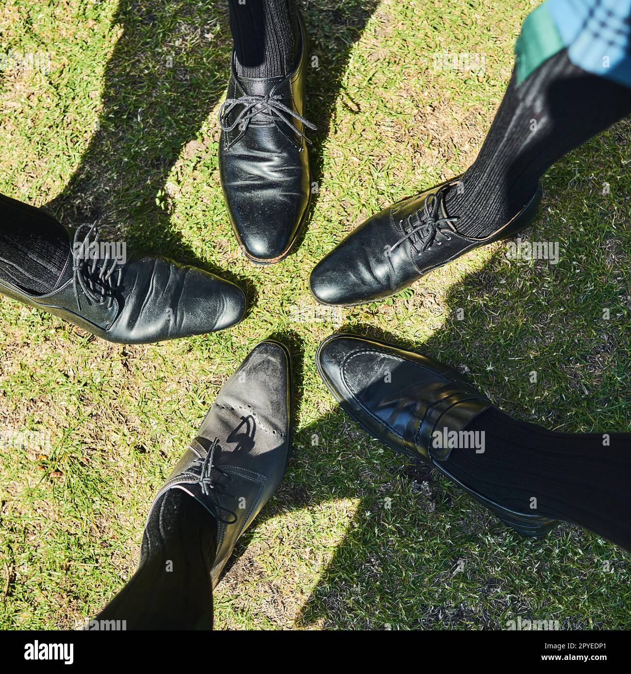 We have matching shoes guys. a group of unrecognizable mens formal dress shoes standing next to each other in a circle outside during the day. Stock Photo