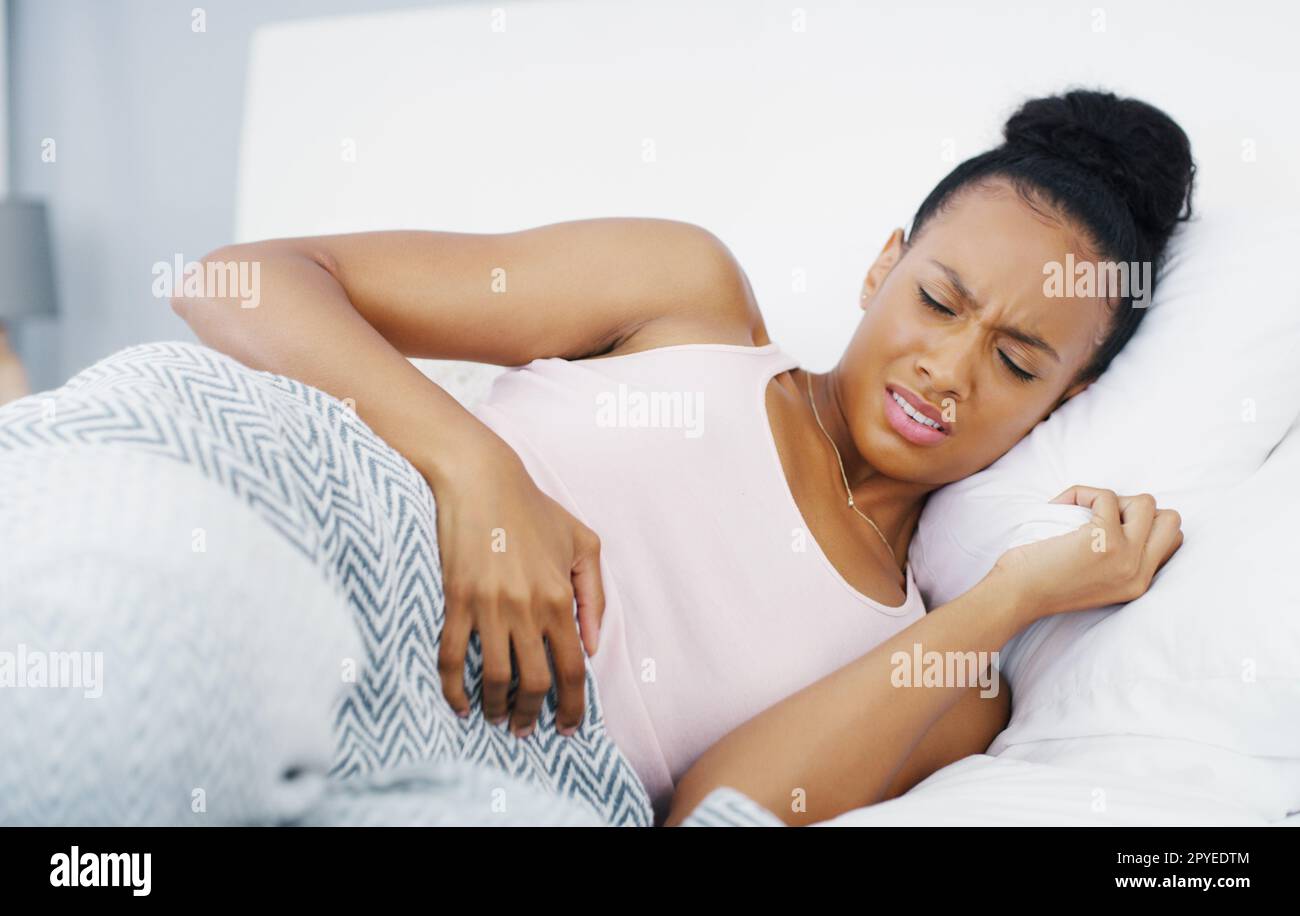 Mother nature is so cruel to us women. an attractive young woman suffering from stomach cramps while lying in her bed at home. Stock Photo