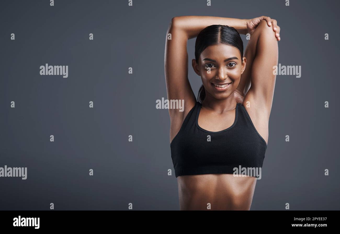 Loosen those muscles for a more relaxed workout. Studio portrait of a sporty young woman stretching her arms against a grey background. Stock Photo