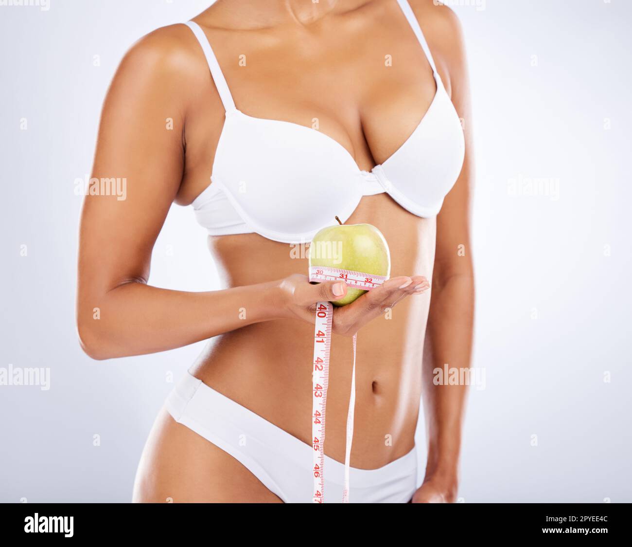 Apple, health and body with woman and fitness, diet and measuring tape with weightloss, detox and fruit against white studio background. Fiber, healthy lifestyle and skin with stomach and underwear. Stock Photo
