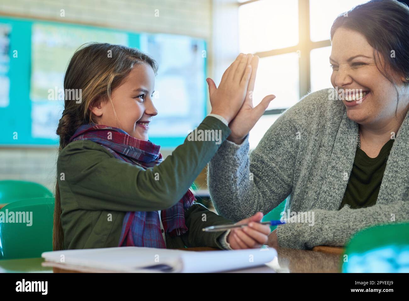 Becoming a top student with the help of her teacher. an elementary school girl high fiving her teacher in class. Stock Photo