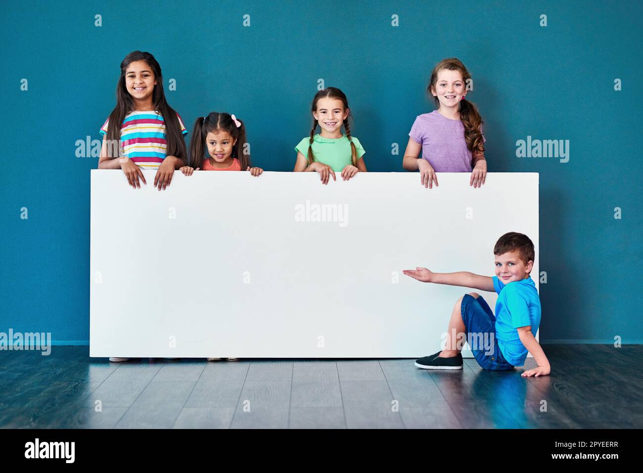 We love it And other kids will too. Studio portrait of a diverse group of kids standing behind a large blank banner against a blue background. Stock Photo