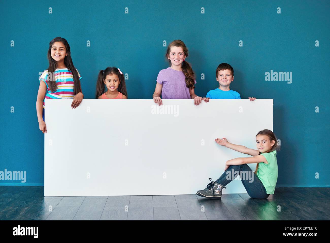 An important message brought to you by the kids. Studio portrait of a diverse group of kids standing behind a large blank banner against a blue background. Stock Photo