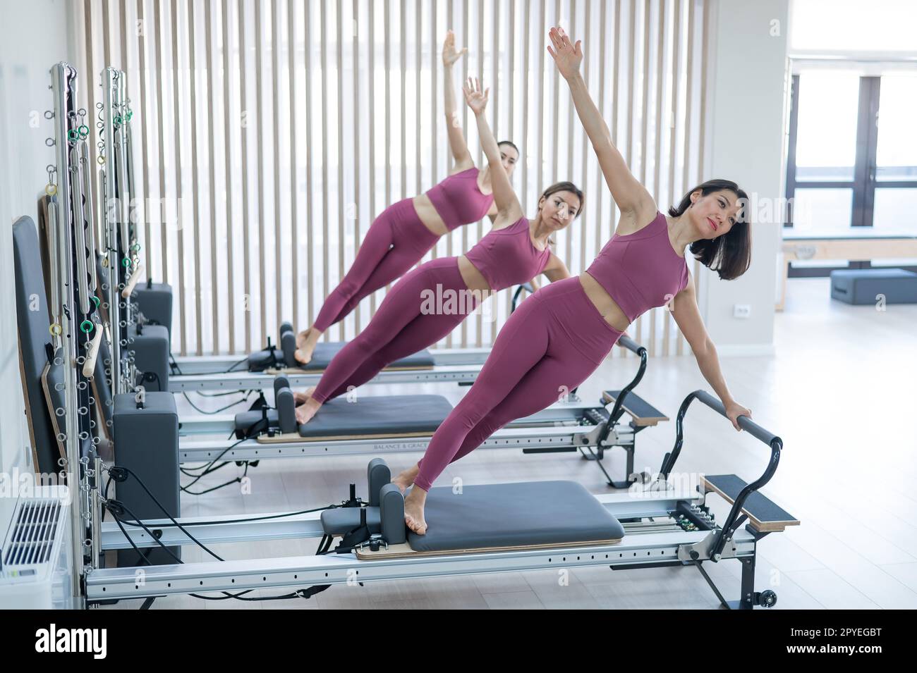 Three Asian women in pink sportswear doing side planks on a reformer