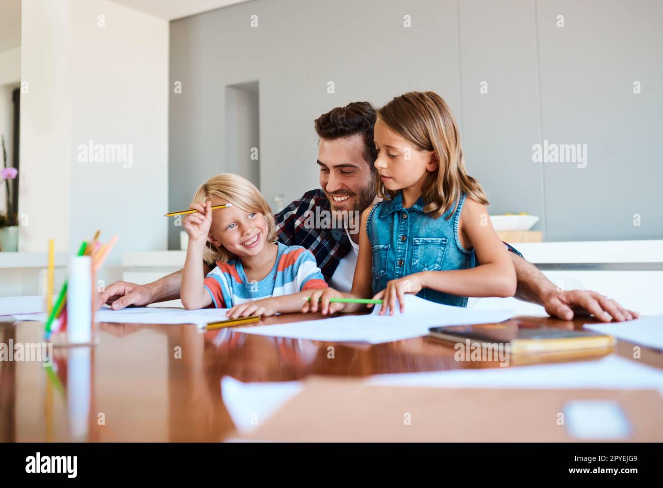 Spending time with them is my favourite activity. a young father helping his two small children with their homework at home. Stock Photo