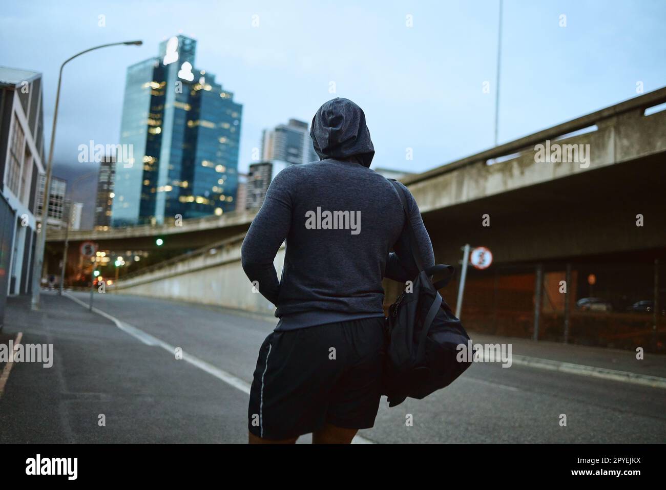 Fitness, running and city with a sports man walking on an asphalt road during an exercise workout. Health, wellness and training with a male runner or athlete in an urban town during the evening Stock Photo