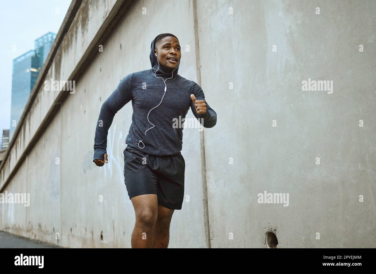 Black man, fitness and running in the city with earphones listening to music during cardio workout. Active African American man runner enjoying audio track, healthy exercise or training in urban town Stock Photo