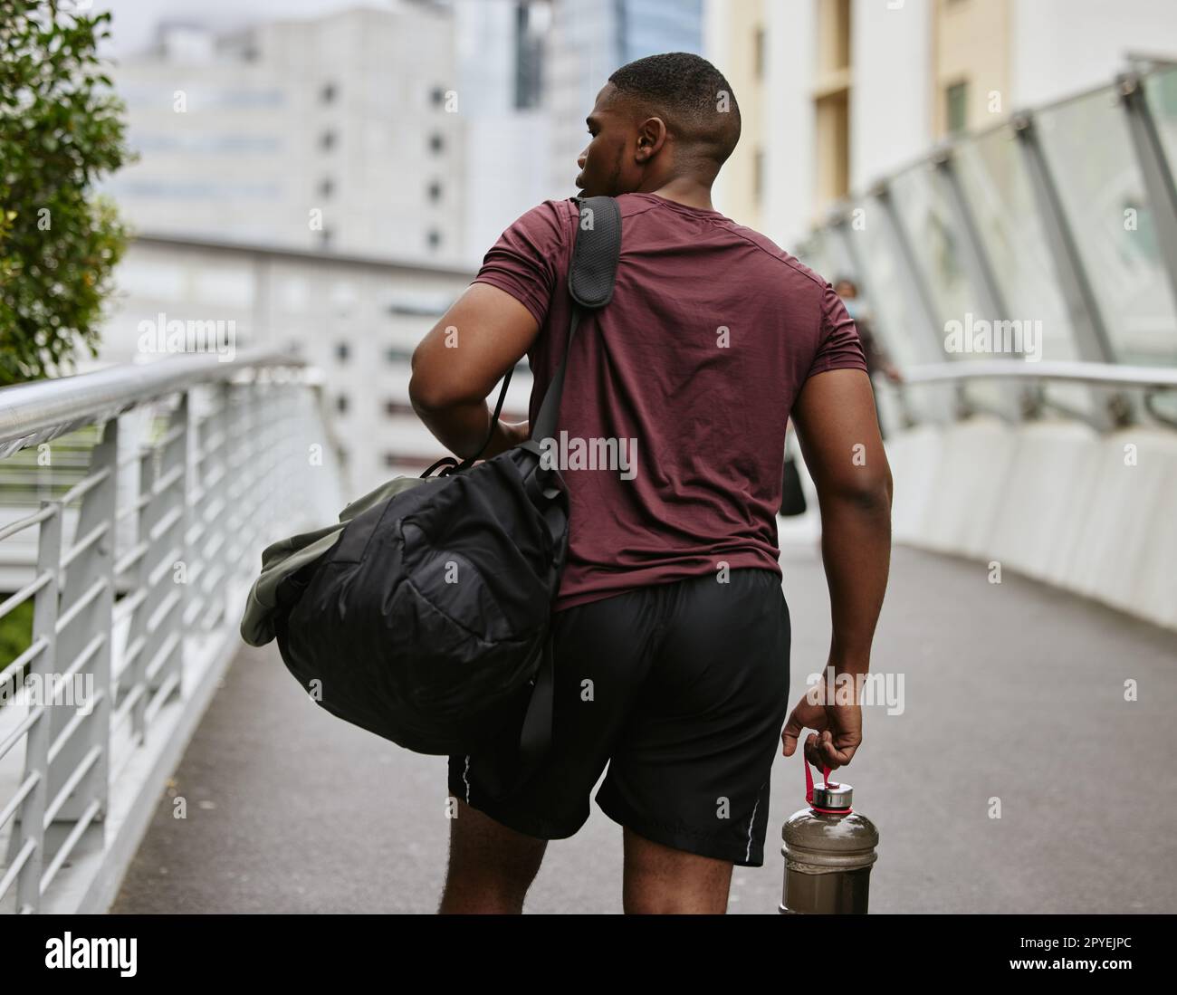 Black man, back or fitness bag on city bridge, road or street with workout gear, training water bottle or exercise kit. Runner, sports athlete or personal trainer in urban travel to gym for wellness Stock Photo