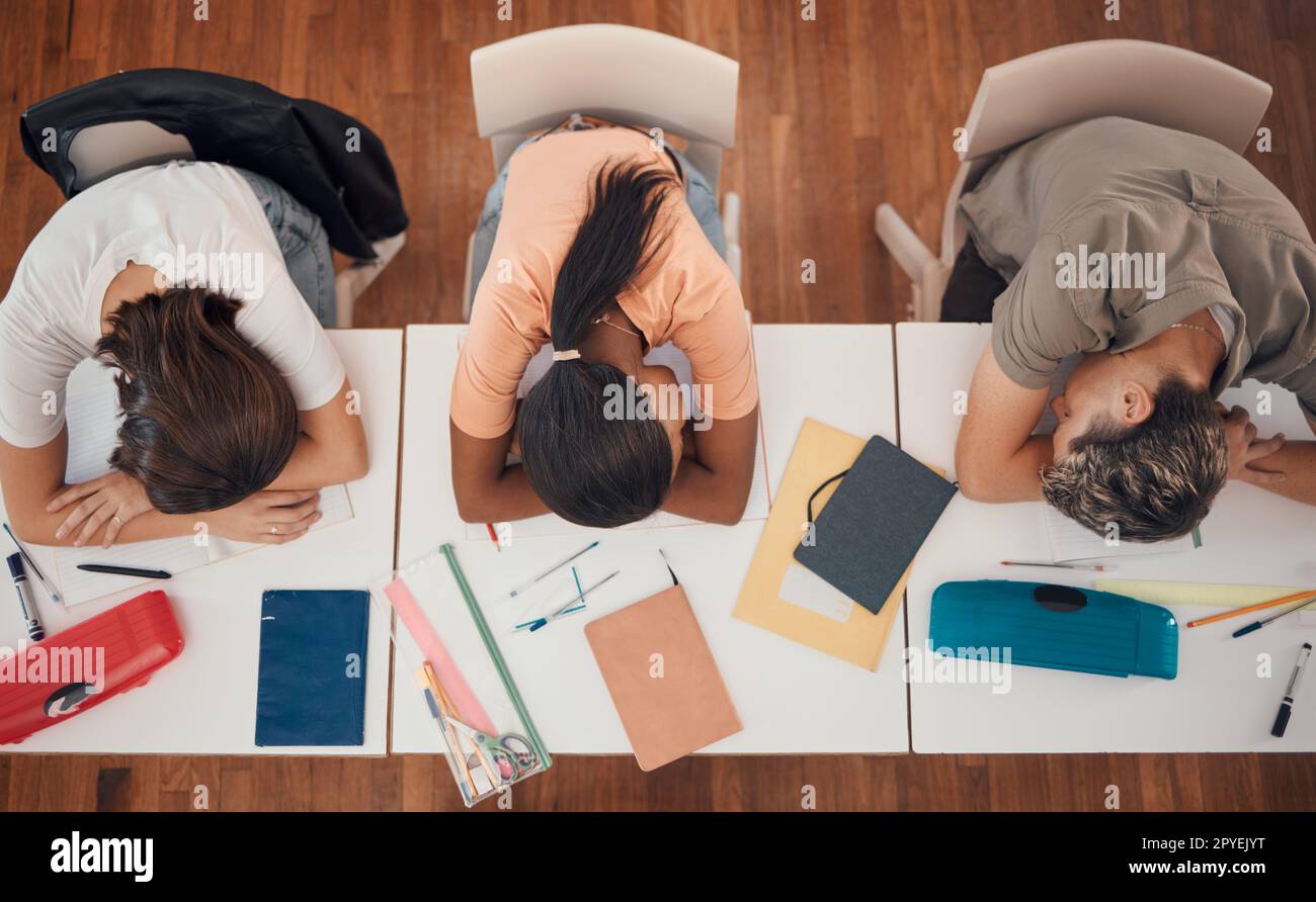 Sleeping, study and desk group students with learning, education and school fatigue, depression or mental health risk. Burnout, stress and tired friends with books on table in library or school above Stock Photo