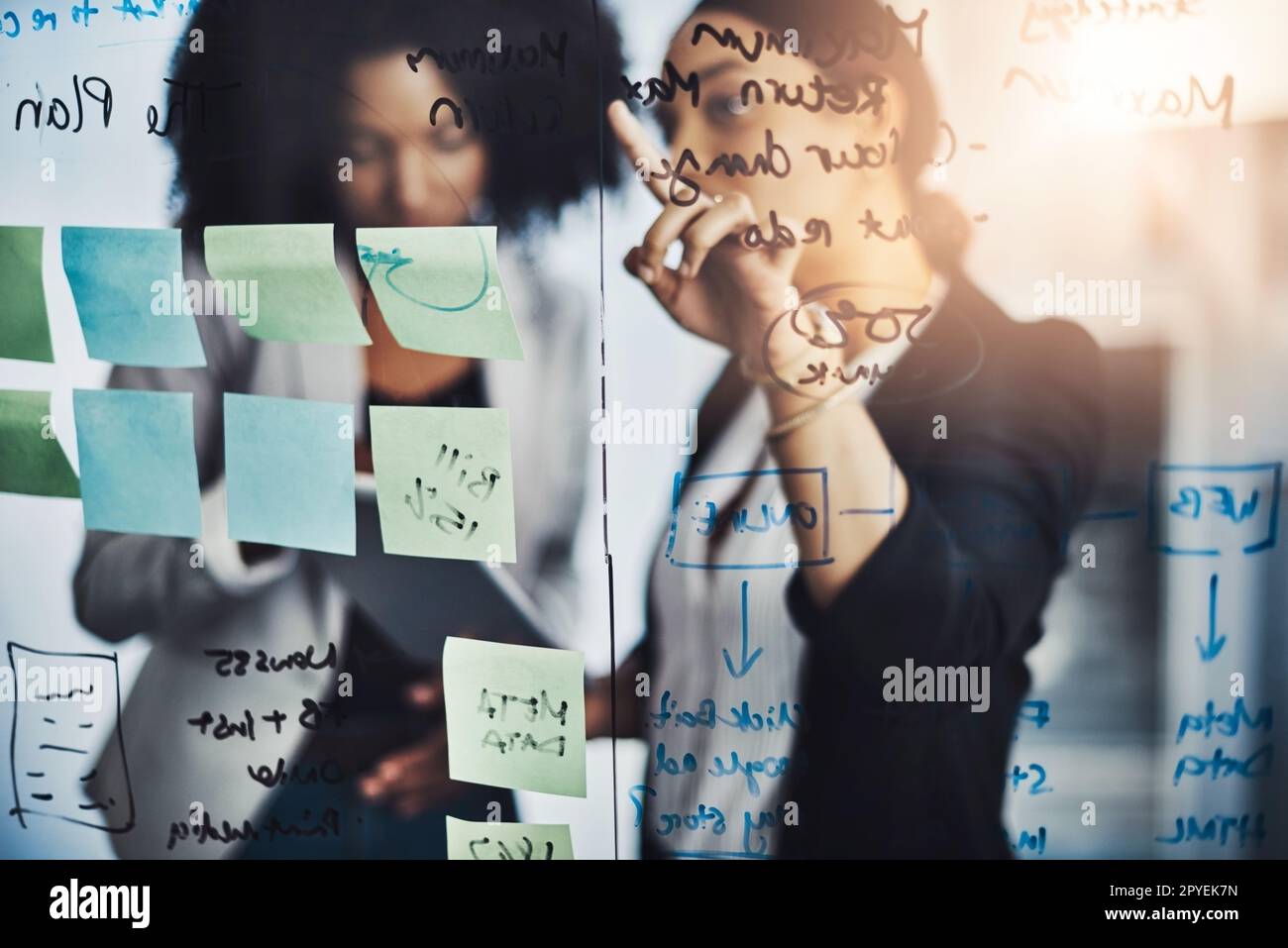 They understand where the bigger picture lies. two businesswomen brainstorming with notes on a glass wall in an office. Stock Photo