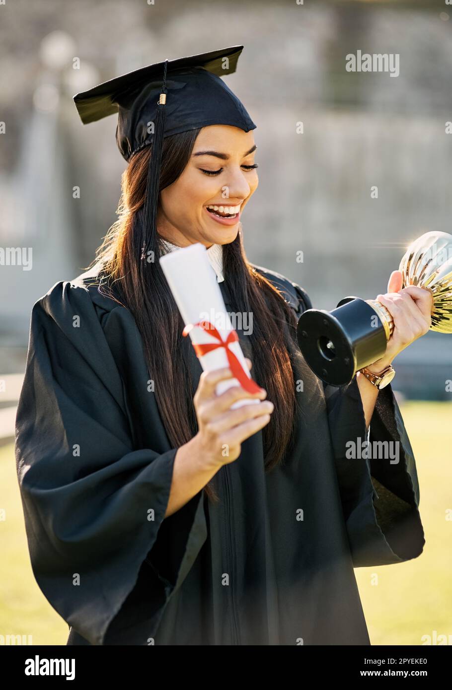 Wow, this is such an honour. a student holding her diploma and trophy on graduation day. Stock Photo