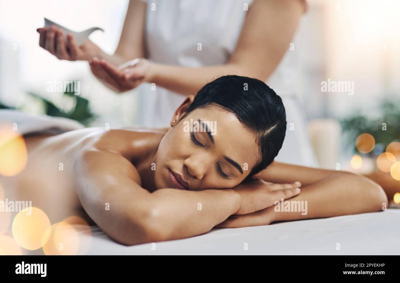 Getting some more oil. a relaxed an cheerful young woman getting a massage indoors at a spa. Stock Photo
