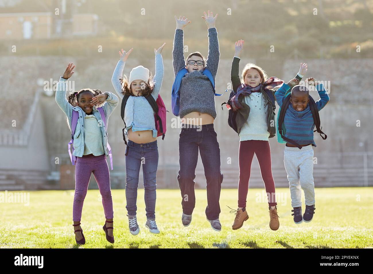 Schools out, time to have fun. elementary school kids jumping outside. Stock Photo