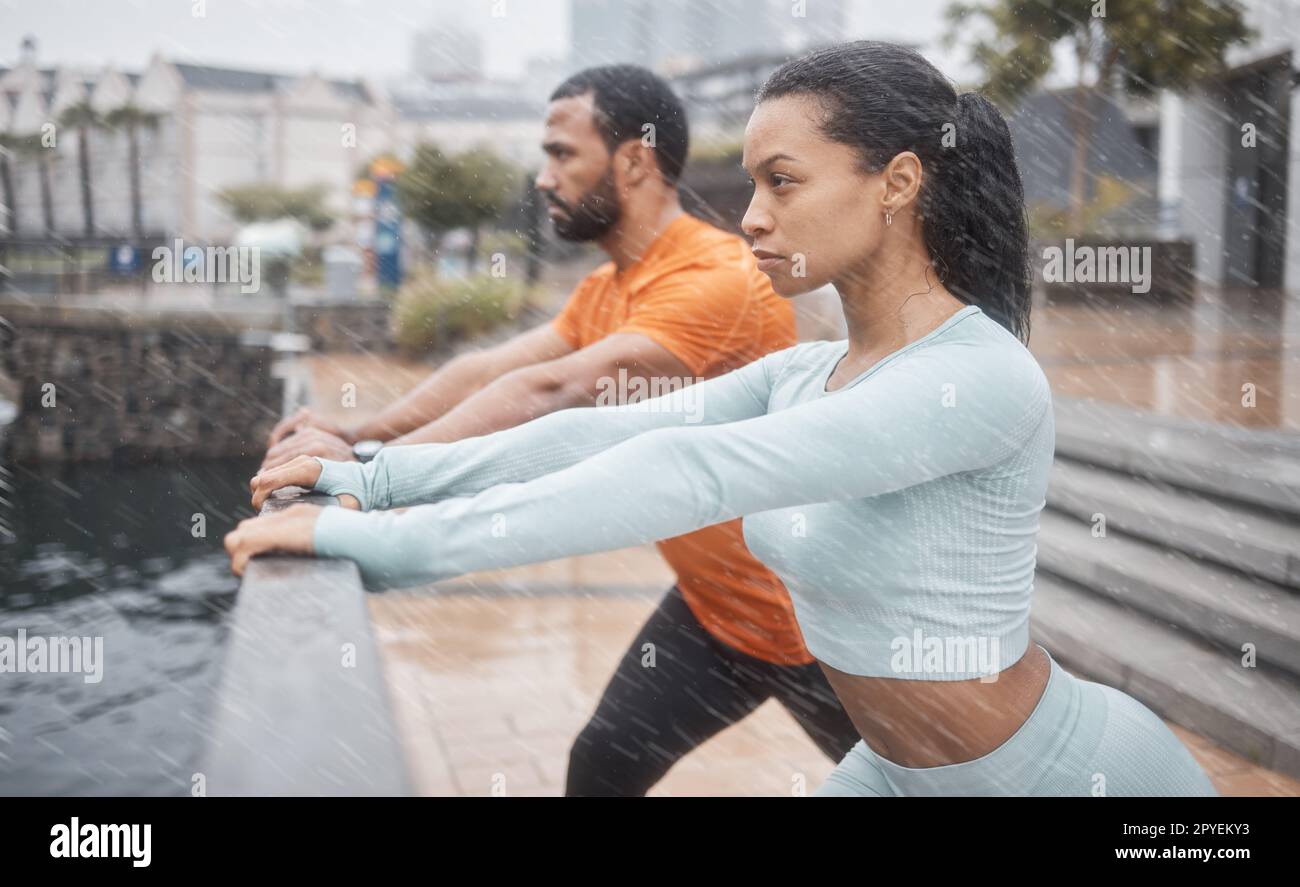 Workout, stretching and couple of friends training with focus before running in the rain. Urban, runner athlete and sports exercise in winter of black people with motivation in the city for fitness Stock Photo