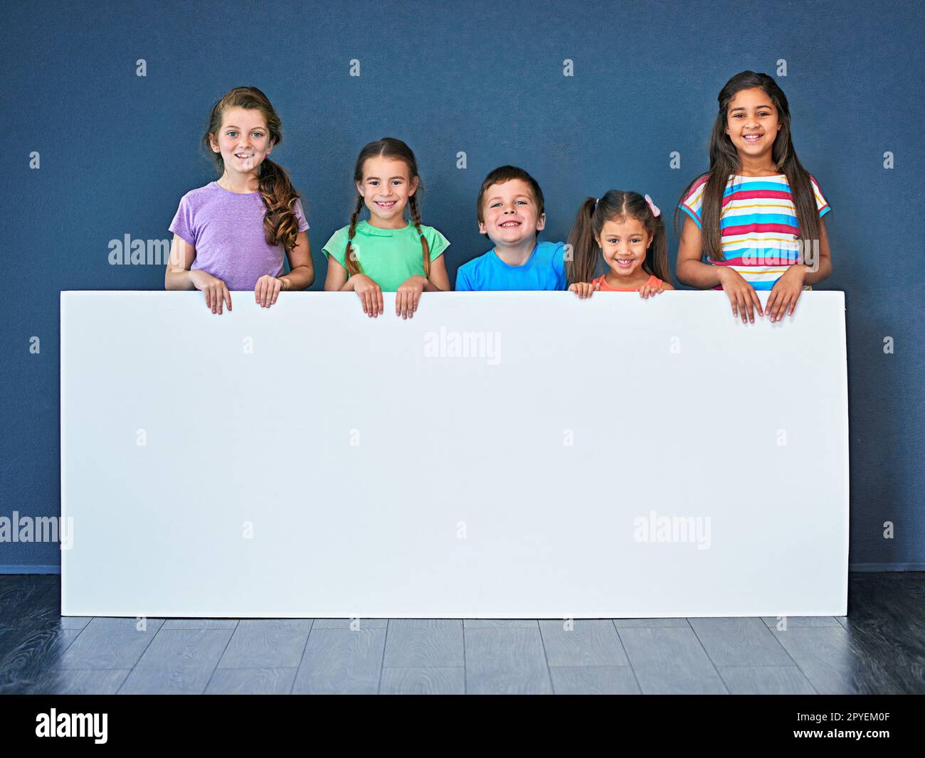 Endorsed by kids for kids. Studio shot of a diverse group of kids standing behind a large blank banner against a blue background. Stock Photo