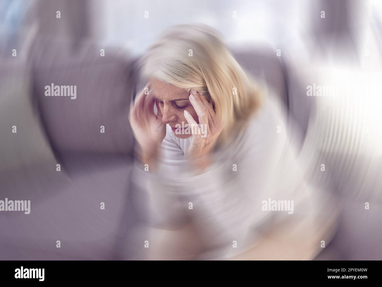 Senior woman, headache and sofa in home with motion blur, pain and depressed while tired in retirement. Elderly, old woman and anxiety with burnout, depression and panic attack on couch at house Stock Photo