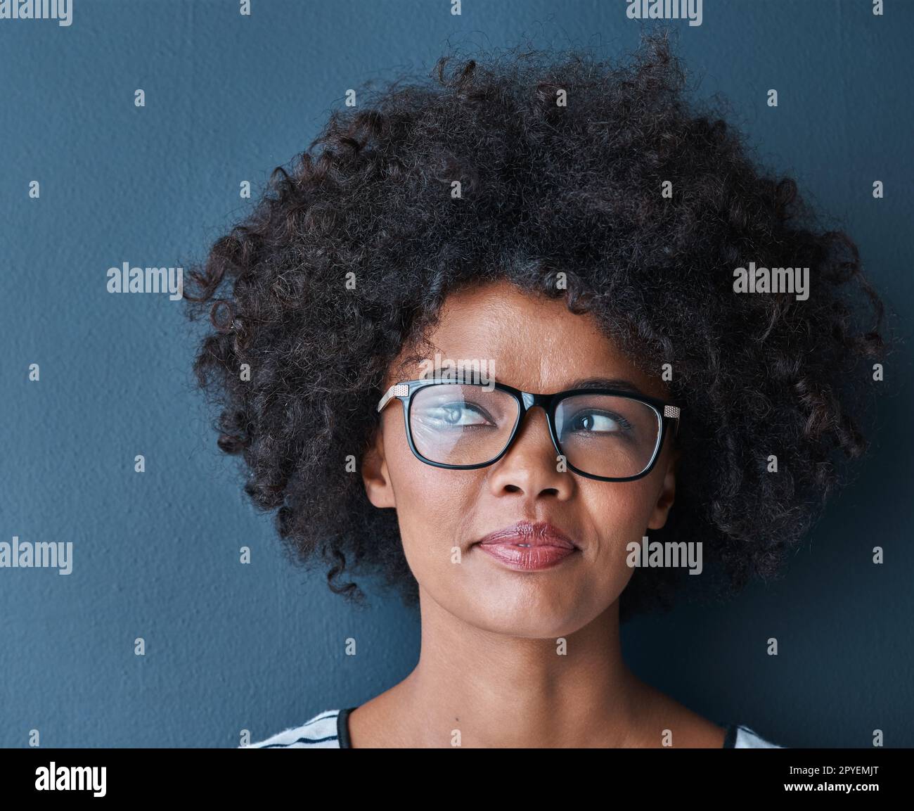 I think Im going to go with that...Studio shot of an attractive young woman wearing glasses and looking thoughtful against a blue background. Stock Photo