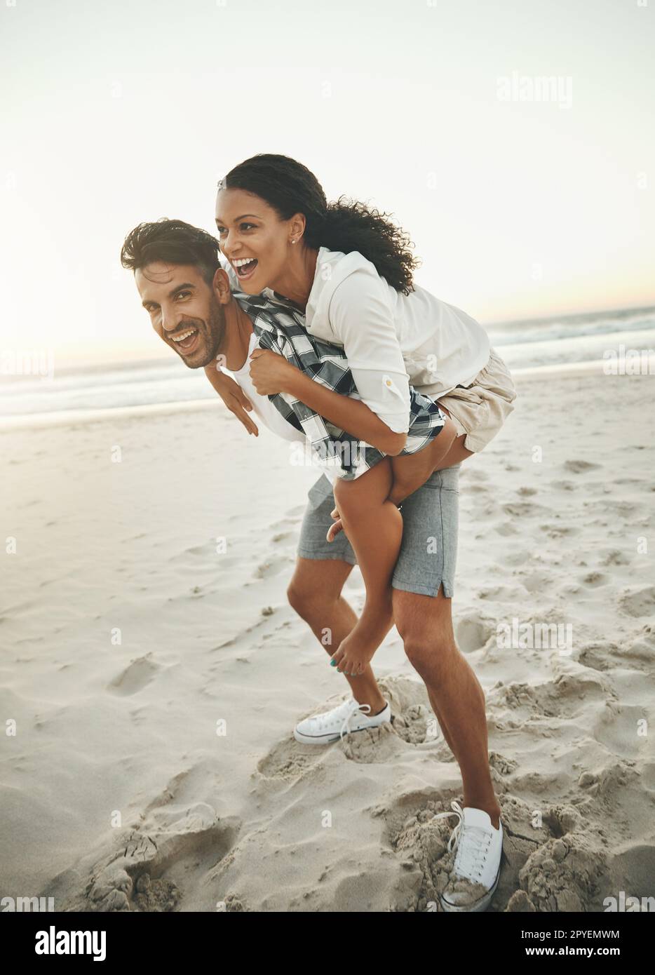 Love makes the world go round. a young man piggybacking his girlfriend while spending the day at the beach. Stock Photo