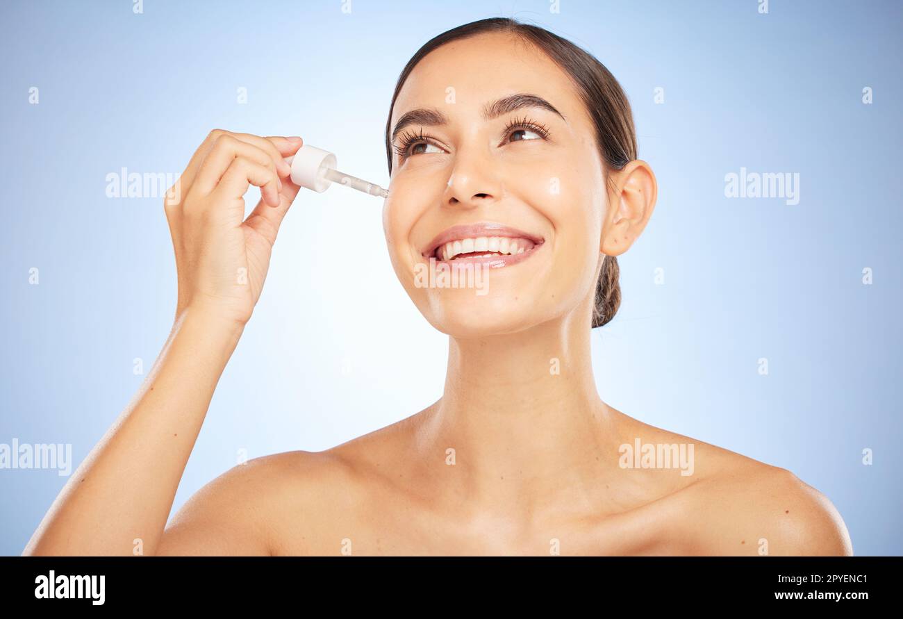 Face, skincare and beauty of woman with serum in studio on a blue background. Thinking, cosmetics or aesthetics of female model with hyaluronic acid, dropper product or essential oil for healthy skin Stock Photo