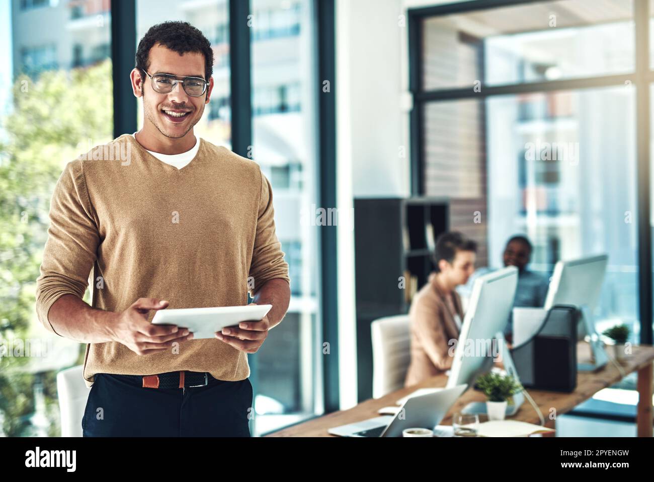Technology can help you achieve your entrepreneurial dreams. a designer using his digital tablet with his colleagues blurred in the background. Stock Photo