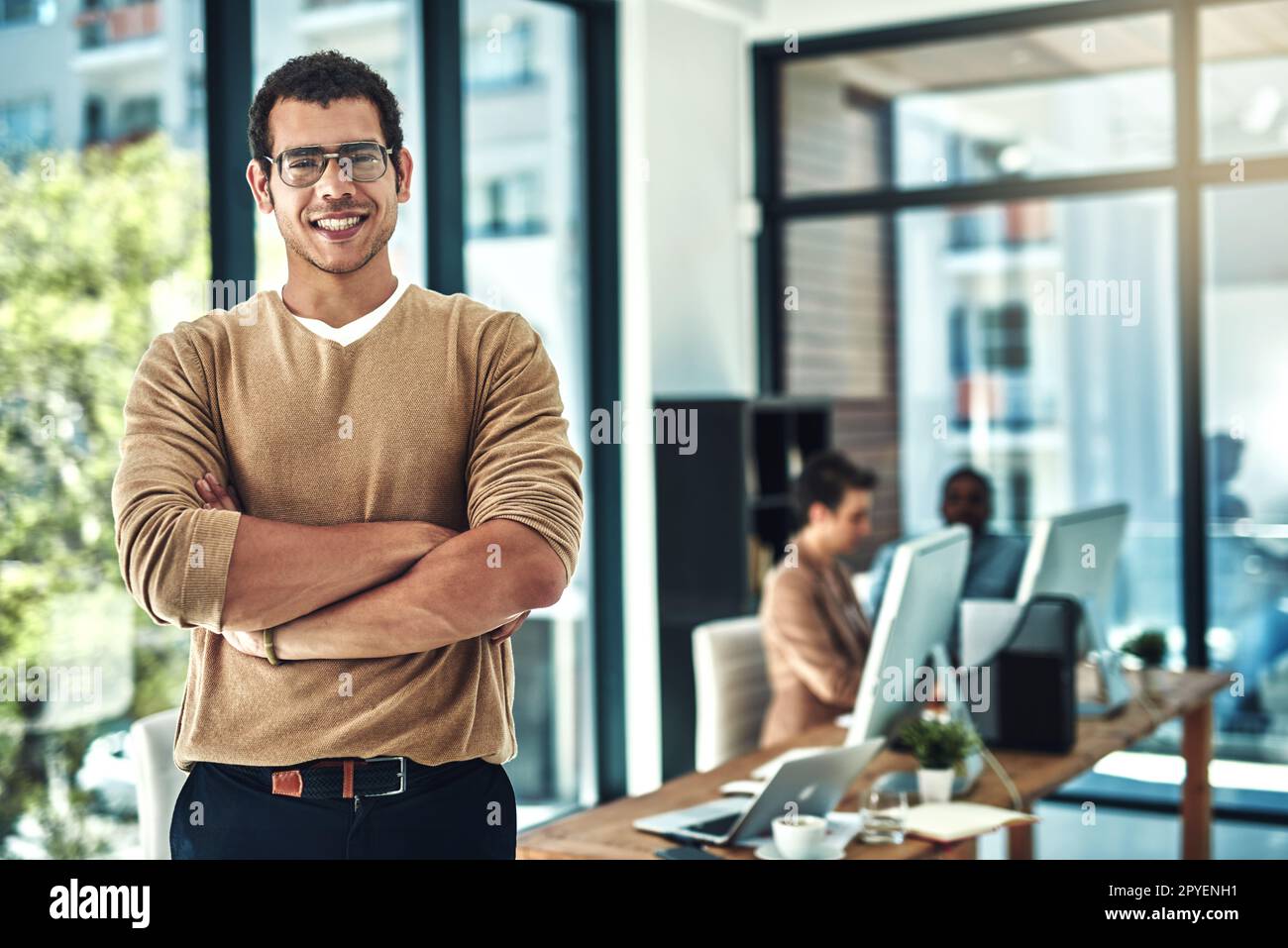 Im finally achieving all my goals. a designer posing in the office with colleagues blurred in the background. Stock Photo