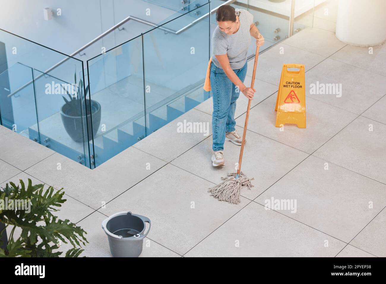 Cleaning service, office building or woman mopping floor with warning sign for job safety compliance. Bucket, bacteria or girl cleaner working on wet floor for dirty, messy or dusty tiles on ground Stock Photo